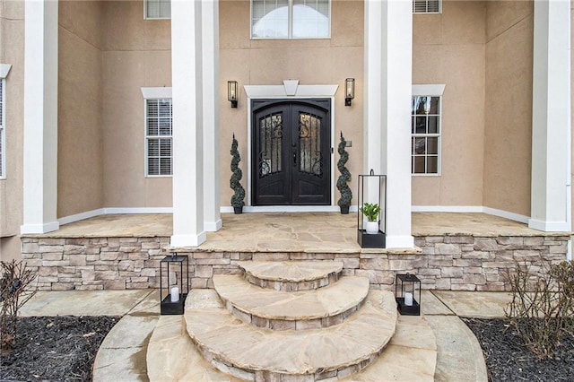 view of exterior entry with stone siding, french doors, visible vents, and stucco siding