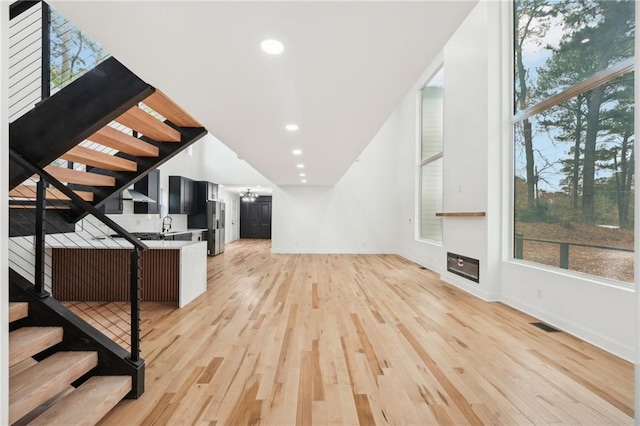 unfurnished living room with a high ceiling, sink, and light hardwood / wood-style flooring