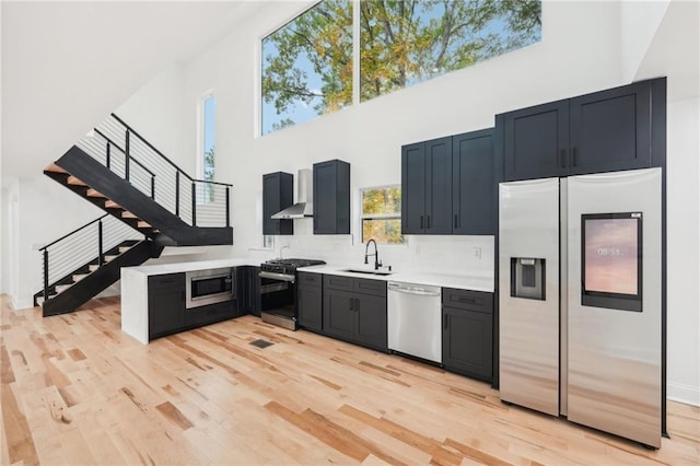 kitchen with stainless steel appliances, a wealth of natural light, and wall chimney range hood