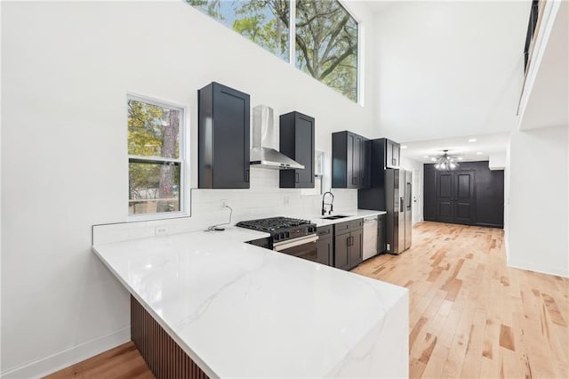 kitchen with stainless steel appliances, a towering ceiling, sink, tasteful backsplash, and light wood-type flooring