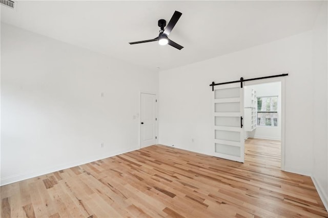 empty room with light wood-type flooring, a barn door, and ceiling fan