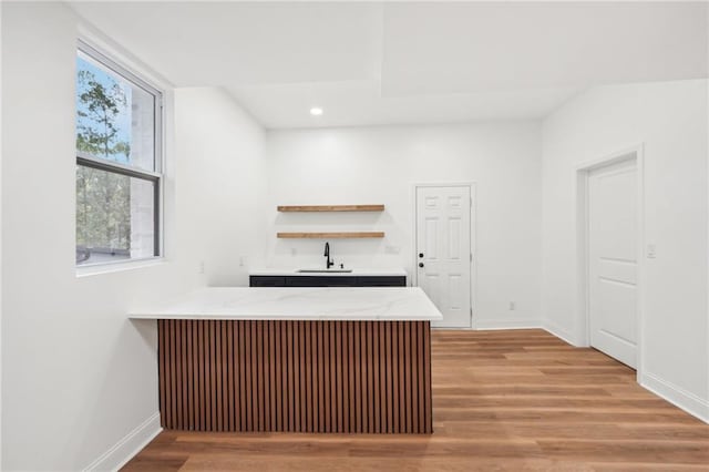 kitchen featuring dark brown cabinetry, light stone countertops, sink, kitchen peninsula, and light hardwood / wood-style flooring