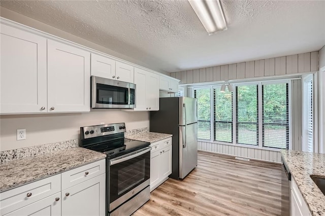 kitchen featuring light wood-type flooring, a textured ceiling, white cabinets, appliances with stainless steel finishes, and light stone countertops