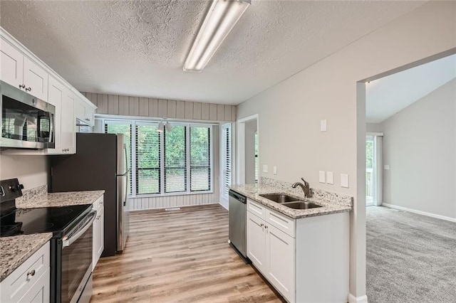 kitchen with white cabinets, light stone countertops, sink, stainless steel appliances, and light wood-type flooring