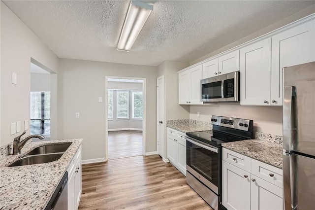 kitchen with light stone counters, sink, white cabinetry, stainless steel appliances, and light hardwood / wood-style floors