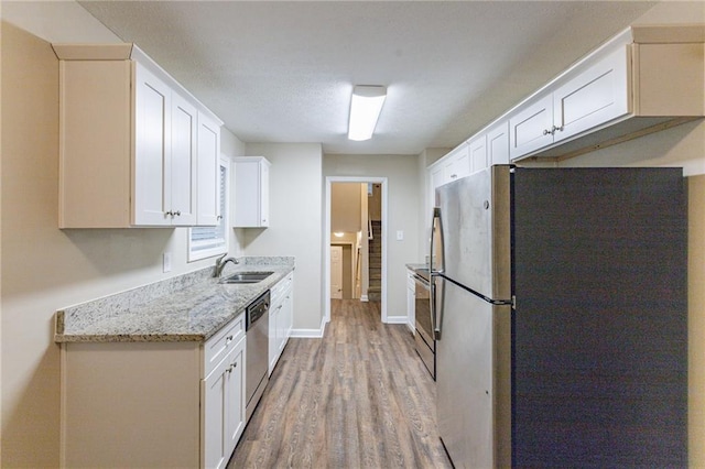 kitchen featuring sink, light hardwood / wood-style flooring, light stone countertops, white cabinetry, and stainless steel appliances