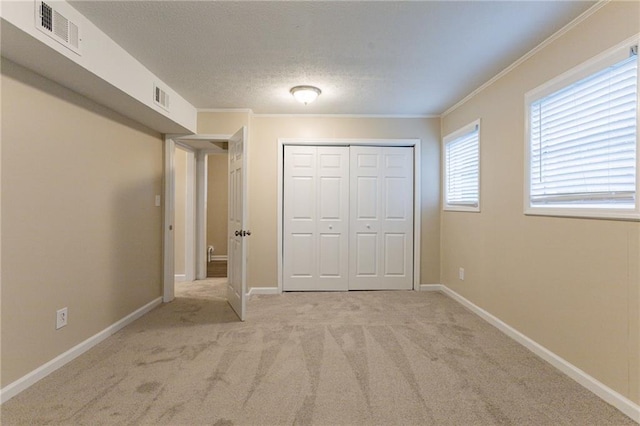 unfurnished bedroom with light carpet, a closet, a textured ceiling, and ornamental molding