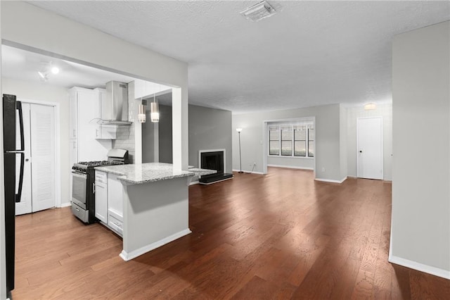 603 Summit N Dr NE Unit 603, Atlanta, GA 30324 - kitchen featuring gas range, wall chimney exhaust hood, white cabinetry, dark wood-type flooring, and light stone counters