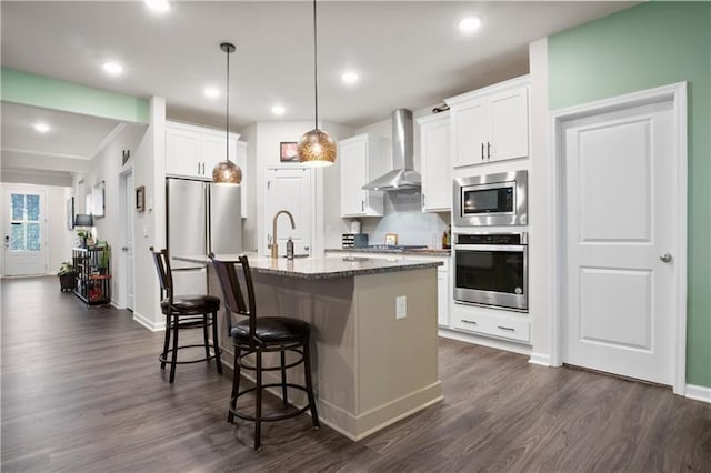 kitchen featuring a breakfast bar, a sink, appliances with stainless steel finishes, wall chimney range hood, and dark wood-style floors