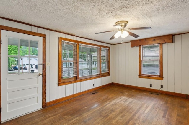 unfurnished room featuring wood-type flooring, healthy amount of natural light, baseboards, a textured ceiling, and crown molding