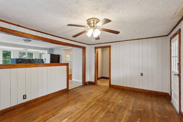 unfurnished room with hardwood / wood-style flooring, a textured ceiling, baseboards, a ceiling fan, and ornamental molding