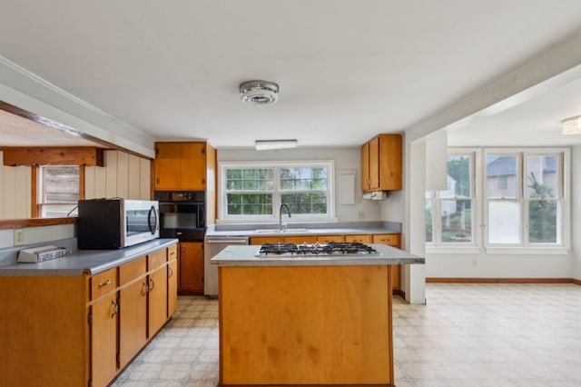 kitchen featuring appliances with stainless steel finishes, a sink, light floors, a kitchen island, and baseboards