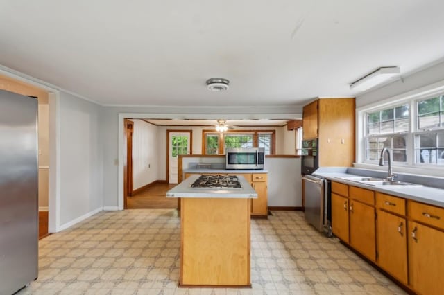 kitchen with appliances with stainless steel finishes, a sink, light countertops, and a kitchen island