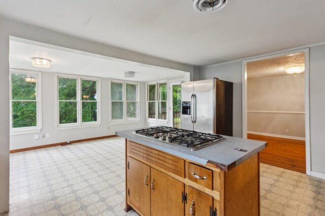 kitchen featuring appliances with stainless steel finishes, light floors, baseboards, a center island, and brown cabinets