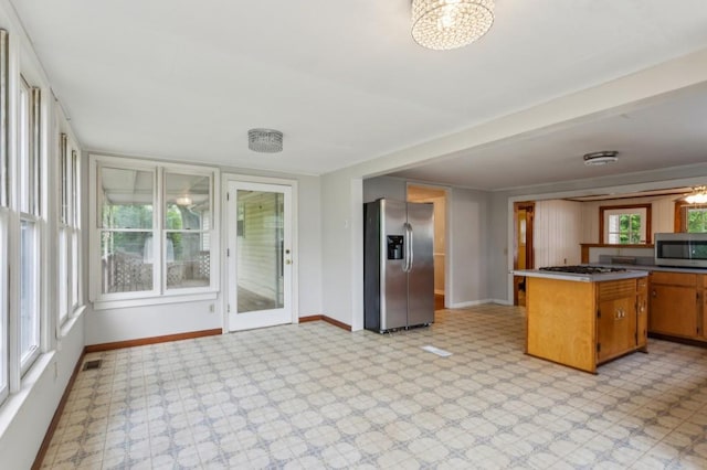 kitchen featuring stainless steel appliances, light floors, baseboards, brown cabinets, and a chandelier