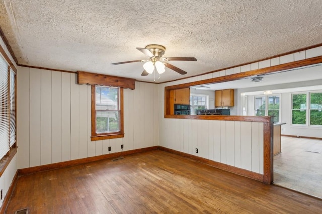 empty room featuring wood-type flooring, plenty of natural light, baseboards, a ceiling fan, and a textured ceiling