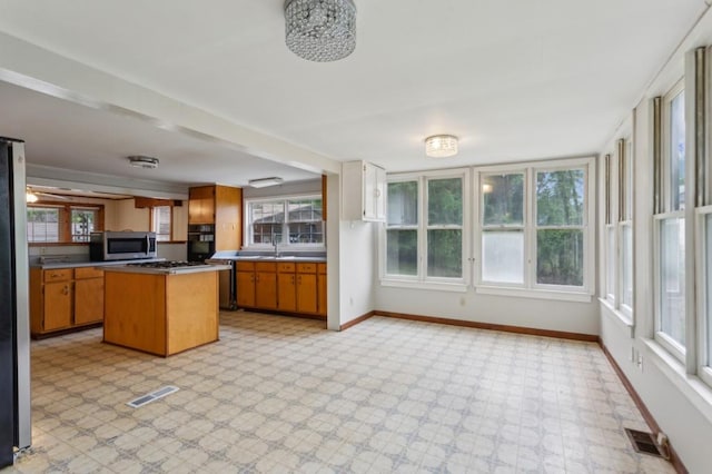 kitchen featuring appliances with stainless steel finishes, baseboards, light floors, brown cabinetry, and a center island