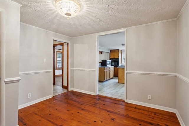 spare room featuring a textured ceiling, wood-type flooring, baseboards, and ornamental molding