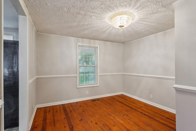 spare room featuring a textured ceiling, hardwood / wood-style flooring, baseboards, and ornamental molding