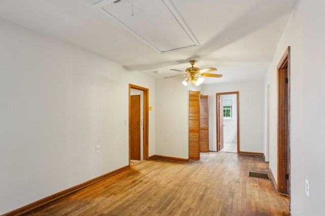 spare room featuring attic access, hardwood / wood-style floors, baseboards, and a ceiling fan