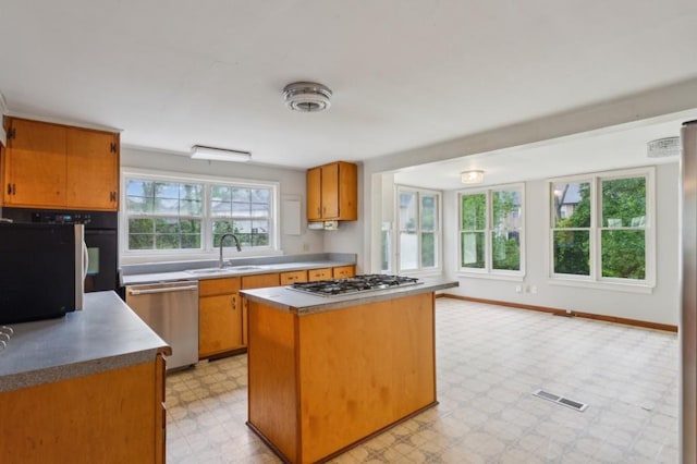 kitchen featuring a sink, stainless steel appliances, light floors, a kitchen island, and brown cabinets