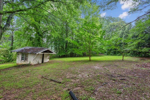 view of grassy yard with a storage unit, an outbuilding, and a forest view