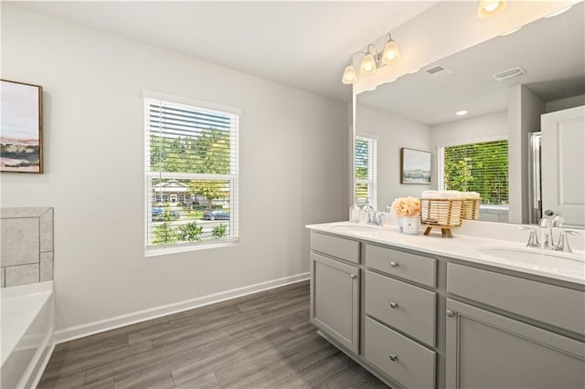 bathroom featuring a tub, dual vanity, hardwood / wood-style floors, and a wealth of natural light