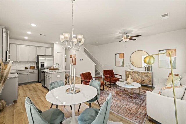 dining room featuring sink, light wood-type flooring, and ceiling fan with notable chandelier