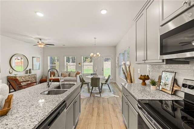 kitchen featuring sink, light wood-type flooring, ceiling fan with notable chandelier, and stainless steel appliances