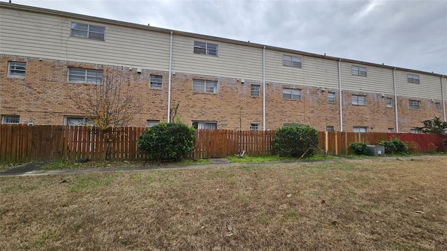 back of property with fence, a lawn, and brick siding