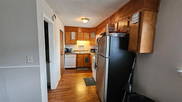 kitchen featuring a textured ceiling, light hardwood / wood-style floors, sink, stainless steel fridge, and white dishwasher