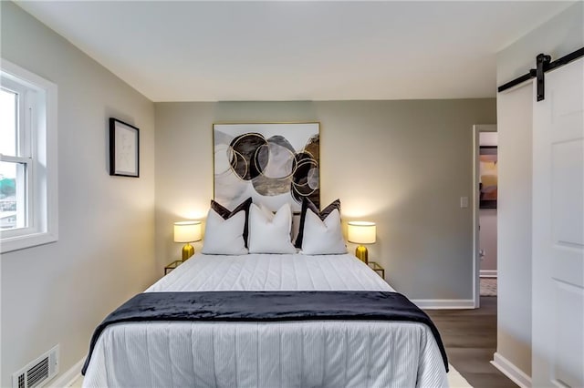 bedroom featuring baseboards, visible vents, a barn door, and wood finished floors