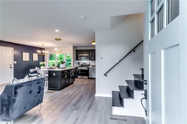 kitchen with a notable chandelier, appliances with stainless steel finishes, dark cabinets, a center island, and a kitchen bar