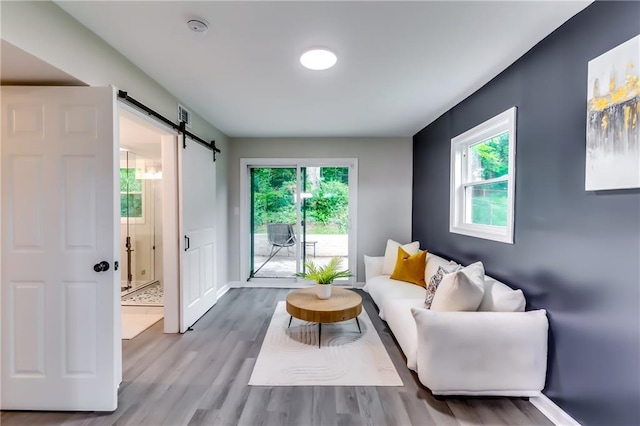 sitting room featuring baseboards, a barn door, wood finished floors, and a healthy amount of sunlight