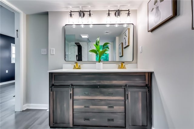 full bath featuring double vanity, wood finished floors, baseboards, an enclosed shower, and a sink