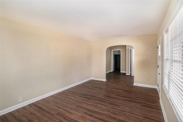 unfurnished room featuring dark wood-type flooring, arched walkways, baseboards, and wallpapered walls