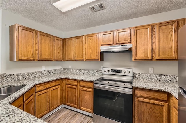 230 Belmont Trl, Covington, GA 30016 - kitchen featuring appliances with stainless steel finishes, under cabinet range hood, brown cabinets, light wood finished floors, and a textured ceiling