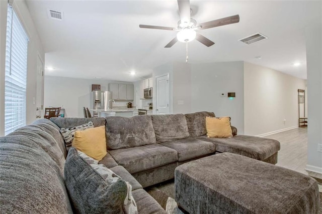 living room with visible vents, baseboards, light wood-style flooring, and a ceiling fan