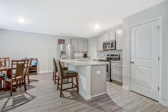 kitchen with a sink, a kitchen bar, appliances with stainless steel finishes, light wood-style floors, and a kitchen island with sink