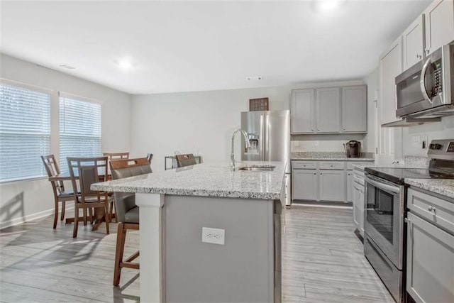 kitchen with a sink, a kitchen breakfast bar, light wood-style floors, stainless steel appliances, and a kitchen island with sink