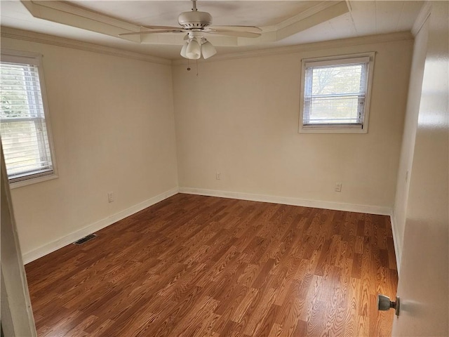 spare room with ornamental molding, a tray ceiling, visible vents, and wood finished floors