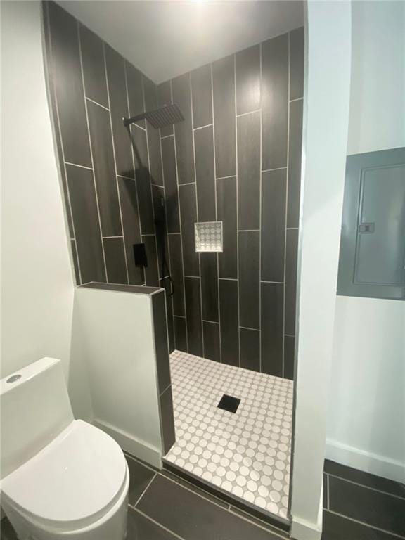 bathroom featuring tile patterned floors, toilet, a tile shower, and electric panel