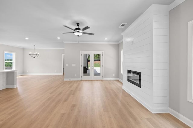 unfurnished living room featuring crown molding, french doors, ceiling fan with notable chandelier, a large fireplace, and light hardwood / wood-style floors