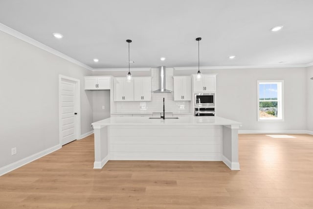 kitchen featuring wall chimney range hood, white cabinetry, a center island with sink, and appliances with stainless steel finishes