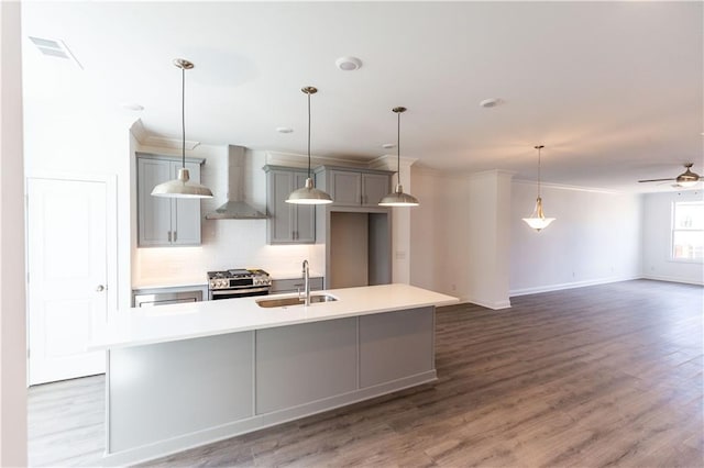 kitchen with stainless steel gas stove, a kitchen island with sink, decorative backsplash, sink, and wall chimney range hood