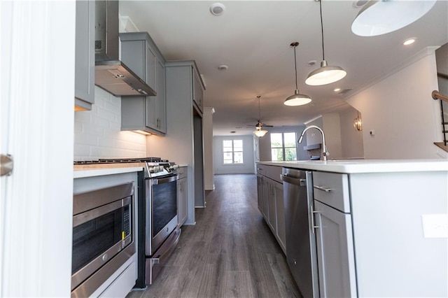 kitchen with pendant lighting, stainless steel appliances, a center island with sink, wall chimney range hood, and decorative backsplash