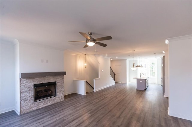 unfurnished living room with dark wood-type flooring, sink, ornamental molding, ceiling fan, and a stone fireplace