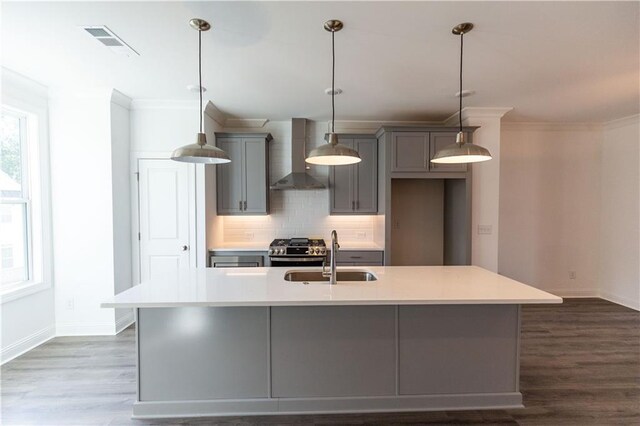 kitchen with sink, decorative light fixtures, wall chimney exhaust hood, gas range, and a kitchen island with sink