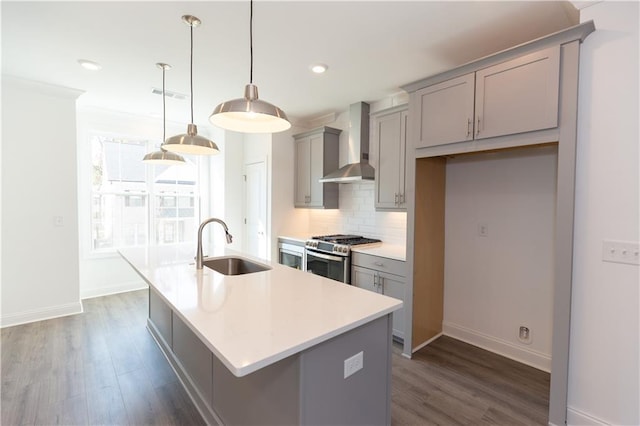 kitchen featuring gas range, pendant lighting, wall chimney range hood, a kitchen island with sink, and sink