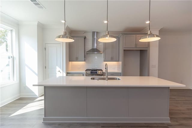 kitchen featuring sink, wall chimney range hood, a kitchen island with sink, and pendant lighting